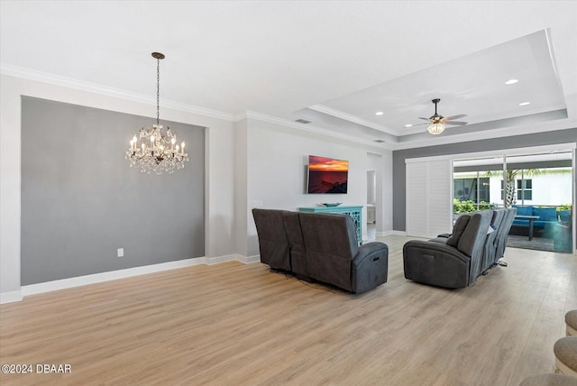 living room featuring light hardwood / wood-style floors, ceiling fan with notable chandelier, crown molding, and a tray ceiling