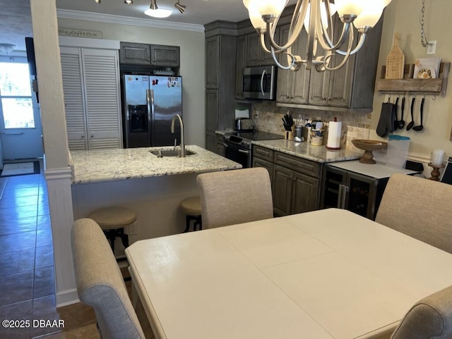 kitchen featuring a notable chandelier, stainless steel appliances, a sink, decorative backsplash, and crown molding