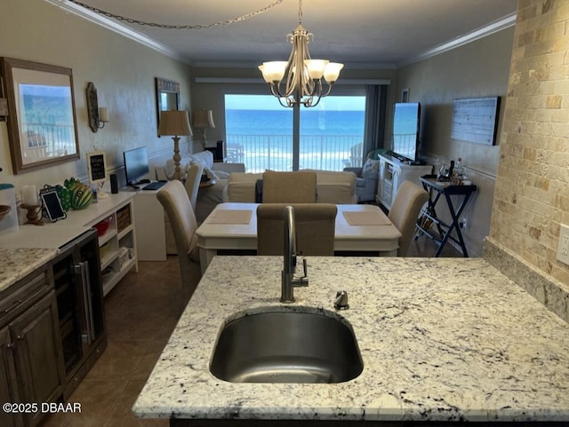 kitchen with crown molding, a chandelier, light stone counters, and a sink