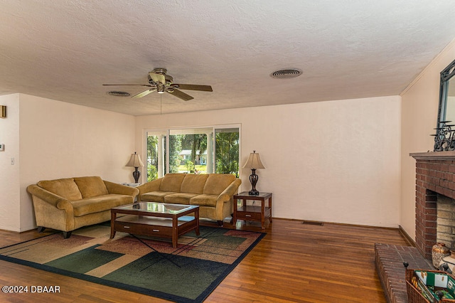 living room featuring a brick fireplace, dark hardwood / wood-style floors, a textured ceiling, and ceiling fan