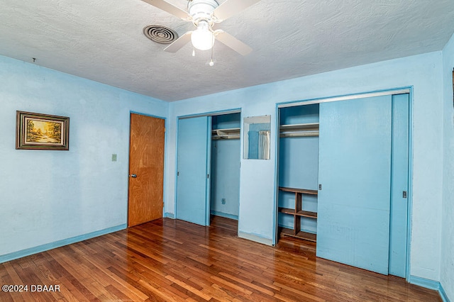 unfurnished bedroom featuring a textured ceiling, two closets, ceiling fan, and dark hardwood / wood-style floors