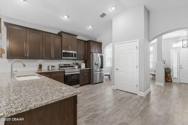 5 Chippeway Ct, Palm Coast, FL 32137 - kitchen with appliances with stainless steel finishes, a sink, arched walkways, dark brown cabinetry, and light stone countertops
