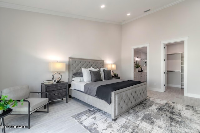 bedroom featuring ensuite bath, a walk in closet, a closet, light wood-type flooring, and crown molding