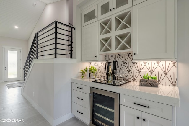 bar featuring wine cooler, white cabinetry, tasteful backsplash, light stone countertops, and lofted ceiling