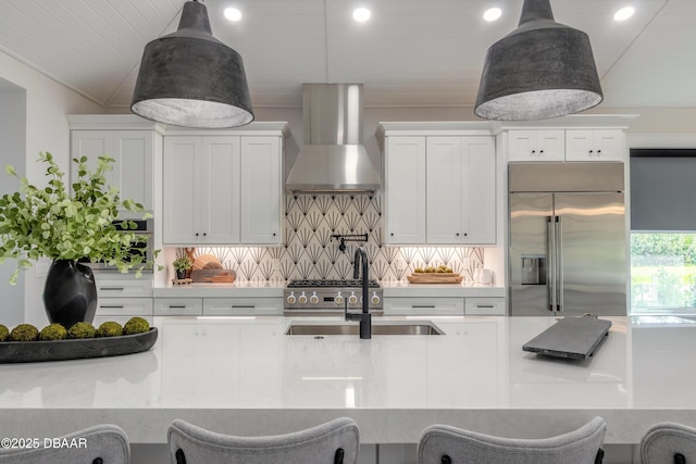 kitchen featuring built in refrigerator, wall chimney exhaust hood, white cabinetry, a kitchen breakfast bar, and backsplash