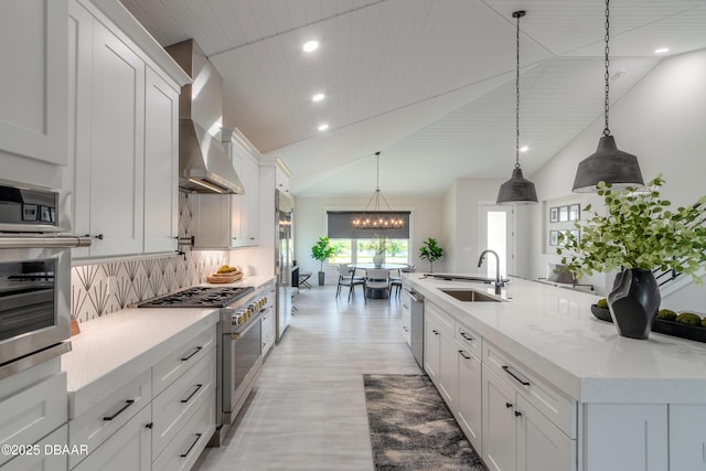 kitchen with appliances with stainless steel finishes, hanging light fixtures, sink, wall chimney range hood, and backsplash