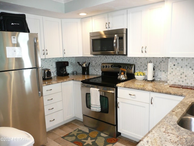 kitchen with stainless steel appliances, white cabinets, backsplash, and light stone counters