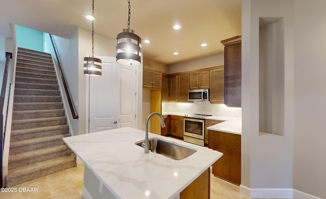 kitchen with sink, light stone counters, hanging light fixtures, a center island with sink, and appliances with stainless steel finishes