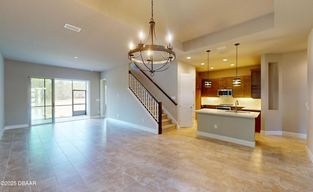 kitchen with sink, backsplash, hanging light fixtures, a kitchen island with sink, and an inviting chandelier