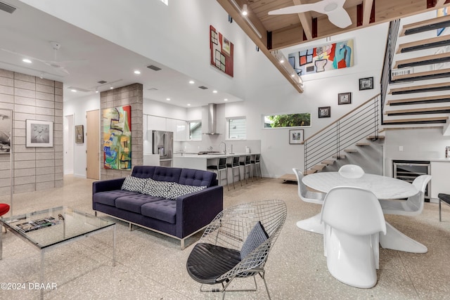 living room with sink, a towering ceiling, ceiling fan, and tile walls