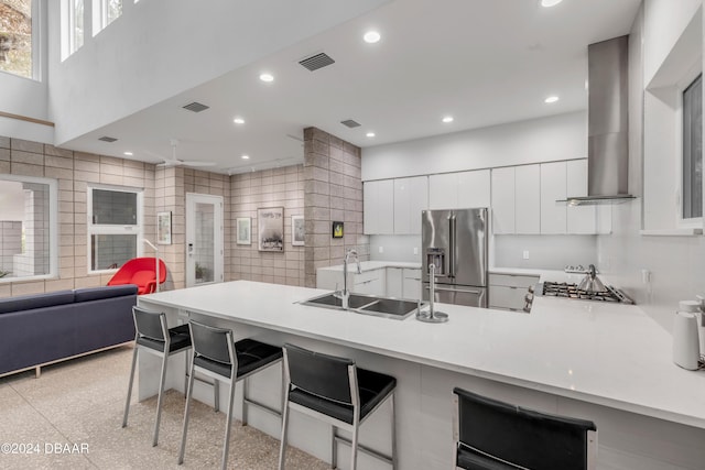 kitchen featuring kitchen peninsula, appliances with stainless steel finishes, sink, wall chimney range hood, and a breakfast bar area