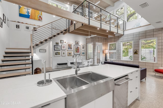 kitchen with sink, stainless steel dishwasher, a towering ceiling, tile walls, and white cabinetry