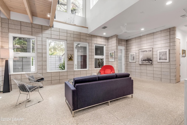 living room with plenty of natural light, ceiling fan, a towering ceiling, and beam ceiling