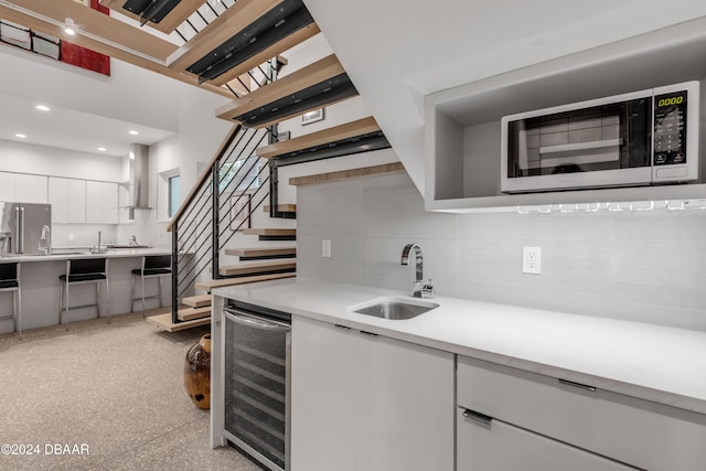 kitchen with white cabinetry, sink, beverage cooler, wall chimney range hood, and stainless steel refrigerator with ice dispenser