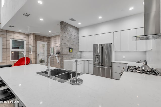 kitchen featuring a breakfast bar, stainless steel appliances, sink, wall chimney range hood, and white cabinetry