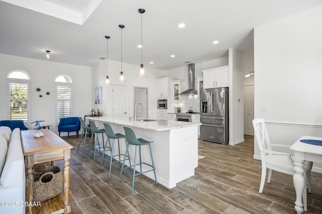 kitchen with pendant lighting, a spacious island, white cabinets, stainless steel appliances, and wall chimney exhaust hood