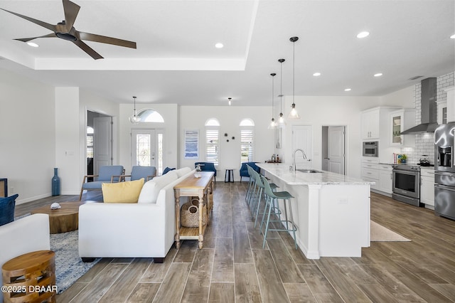 kitchen featuring appliances with stainless steel finishes, pendant lighting, white cabinetry, a spacious island, and wall chimney exhaust hood