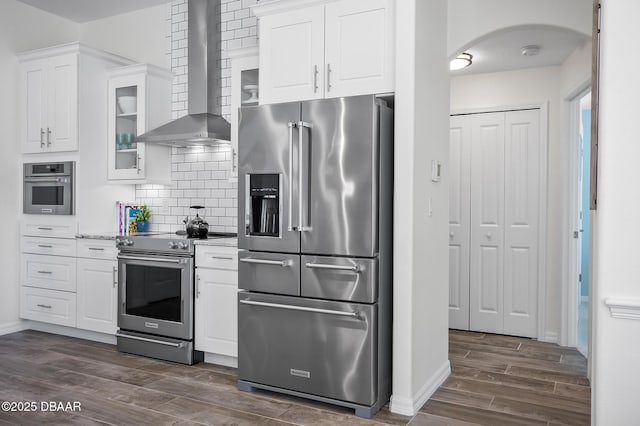 kitchen with white cabinetry, backsplash, high quality appliances, light stone counters, and wall chimney exhaust hood