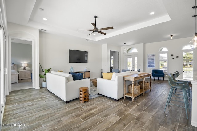 living room with a tray ceiling, ceiling fan with notable chandelier, and french doors