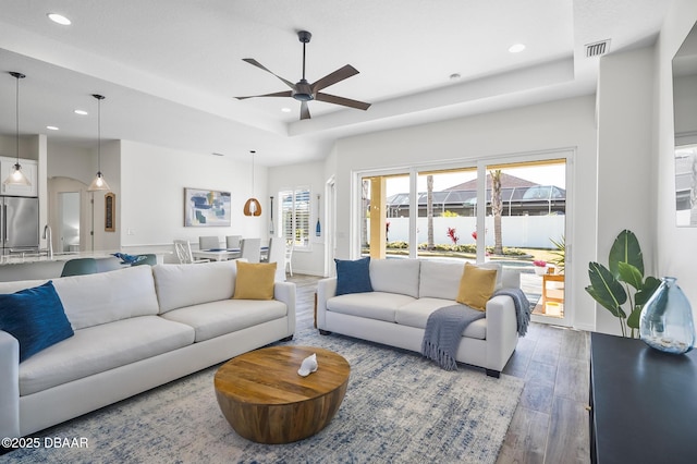 living room featuring sink, a tray ceiling, dark hardwood / wood-style floors, and a healthy amount of sunlight