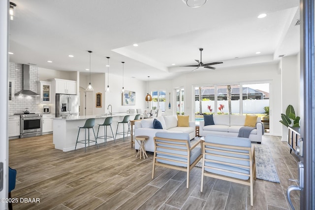 living room featuring sink, a raised ceiling, and ceiling fan