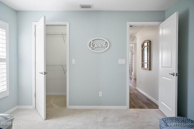 bedroom with a walk in closet, a closet, and light carpet