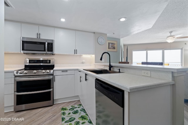 kitchen with a sink, light countertops, light wood finished floors, a peninsula, and stainless steel appliances