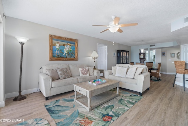 living room featuring baseboards, ceiling fan, light wood-style flooring, and visible vents