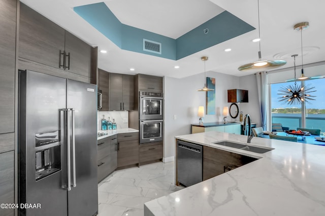 kitchen with appliances with stainless steel finishes, dark brown cabinetry, light stone countertops, hanging light fixtures, and sink