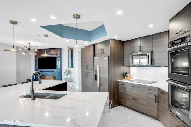 kitchen featuring stainless steel appliances, sink, decorative light fixtures, and light stone counters