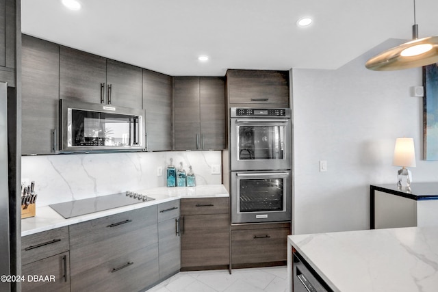 kitchen featuring stainless steel appliances, dark brown cabinetry, light stone countertops, hanging light fixtures, and decorative backsplash