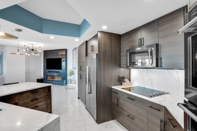 kitchen with appliances with stainless steel finishes, tasteful backsplash, an inviting chandelier, hanging light fixtures, and a fireplace