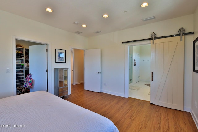 bedroom featuring ensuite bath, a barn door, hardwood / wood-style floors, and a walk in closet