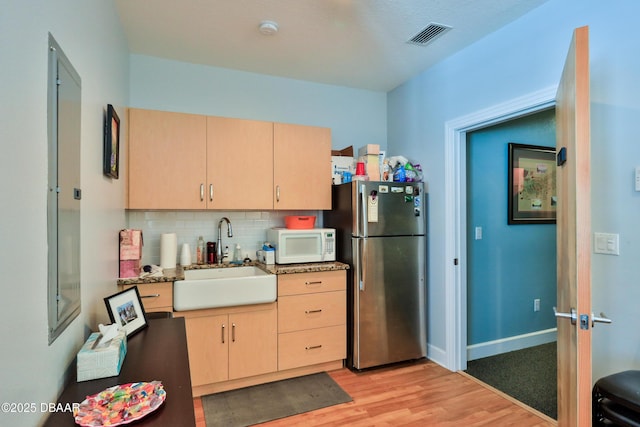 kitchen featuring sink, stainless steel refrigerator, backsplash, light hardwood / wood-style floors, and light brown cabinetry