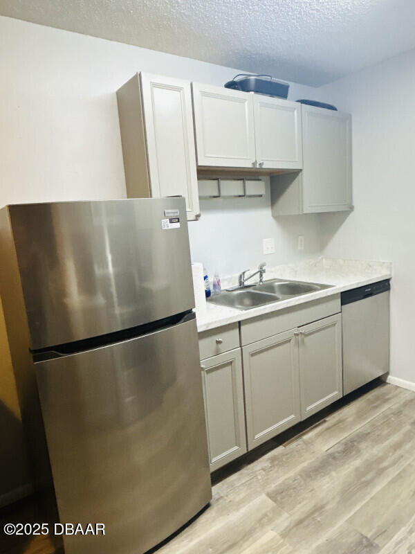 kitchen with sink, gray cabinets, appliances with stainless steel finishes, light hardwood / wood-style floors, and a textured ceiling