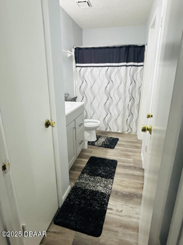 bathroom with walk in shower, toilet, a textured ceiling, vanity, and hardwood / wood-style floors