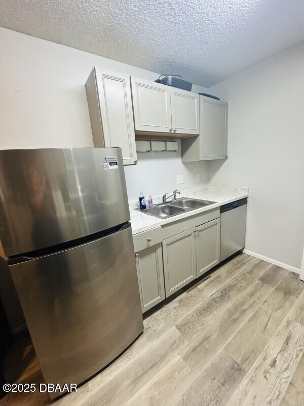 kitchen featuring sink, gray cabinetry, light wood-type flooring, stainless steel appliances, and a textured ceiling