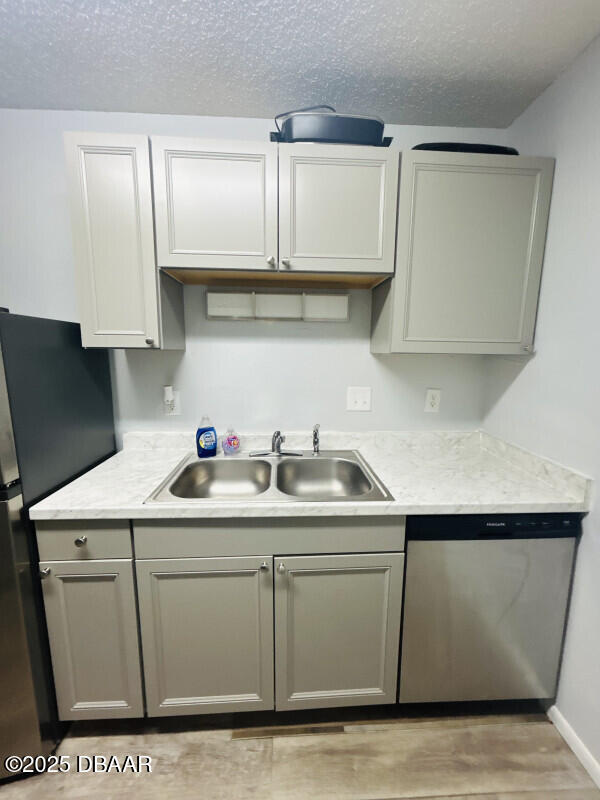 kitchen with appliances with stainless steel finishes, sink, a textured ceiling, and light wood-type flooring