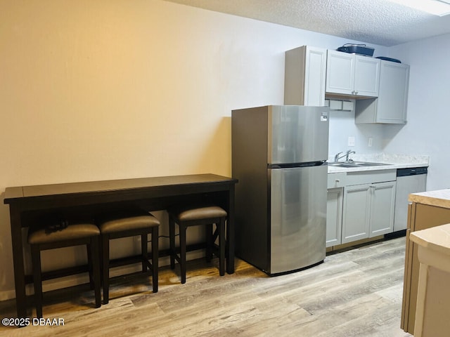 kitchen with sink, a textured ceiling, light wood-type flooring, appliances with stainless steel finishes, and gray cabinets