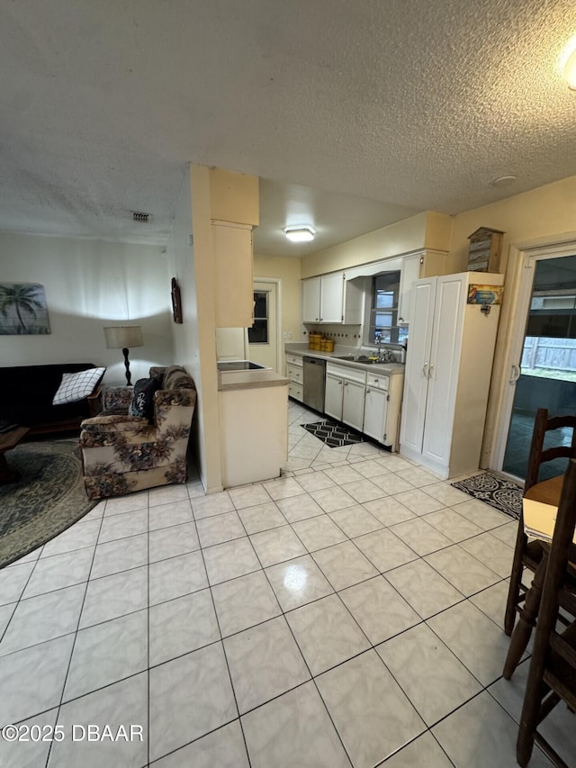 kitchen featuring a sink, dishwasher, light countertops, a textured ceiling, and light tile patterned floors