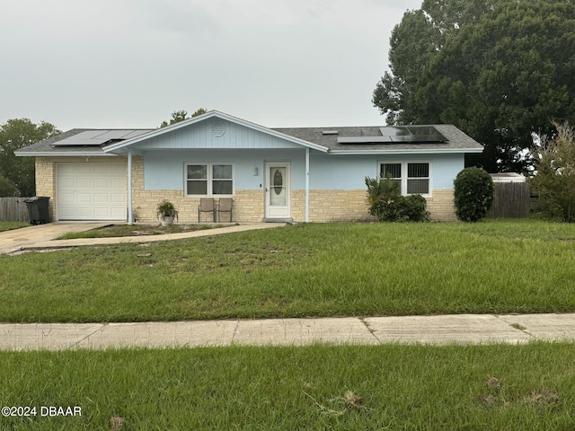 single story home with a garage, driveway, solar panels, and a front lawn