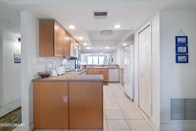 kitchen with white appliances, a peninsula, recessed lighting, a raised ceiling, and light tile patterned flooring