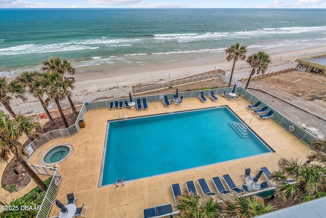 community pool featuring view of water and beach, fence, and a patio area