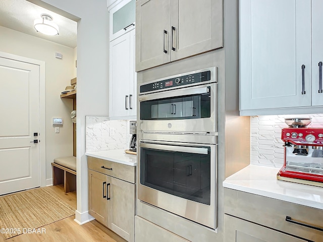 kitchen featuring light countertops, light wood finished floors, stainless steel double oven, and backsplash