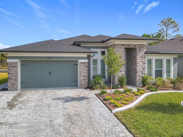 prairie-style house with a garage, a shingled roof, decorative driveway, and a front yard