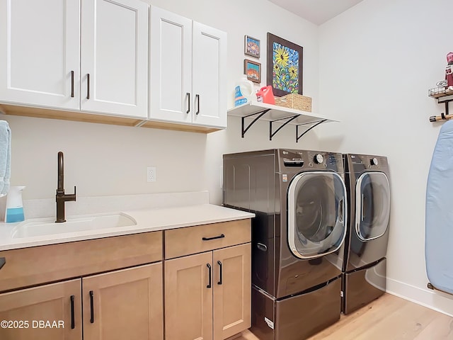 washroom featuring cabinet space, baseboards, washing machine and clothes dryer, light wood-type flooring, and a sink