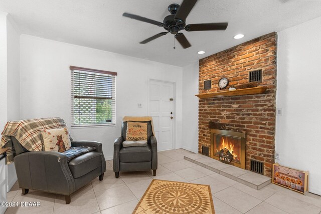 sitting room featuring a textured ceiling, light tile patterned floors, ceiling fan, and a brick fireplace