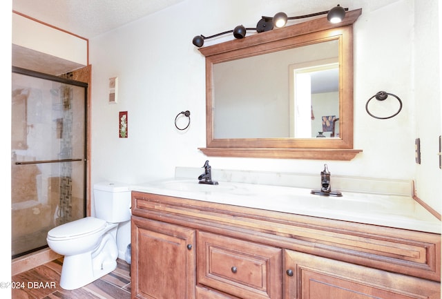 bathroom featuring a textured ceiling, wood-type flooring, vanity, a shower with shower door, and toilet