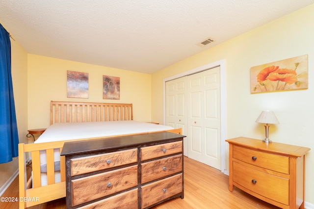 bedroom with light hardwood / wood-style flooring, a textured ceiling, and a closet