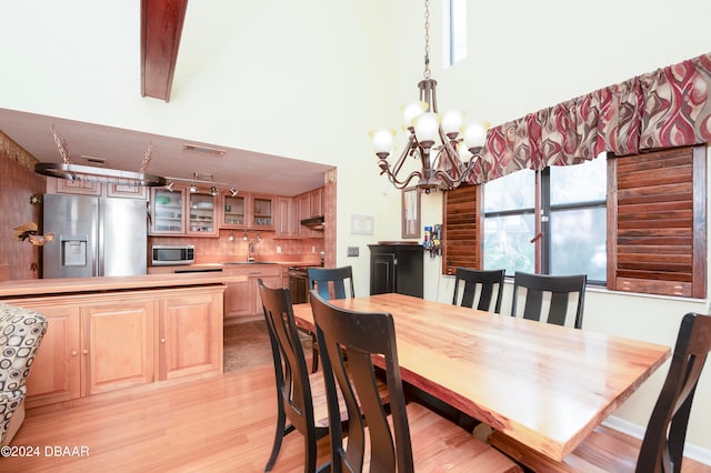 dining area with a high ceiling, a chandelier, sink, and light hardwood / wood-style floors